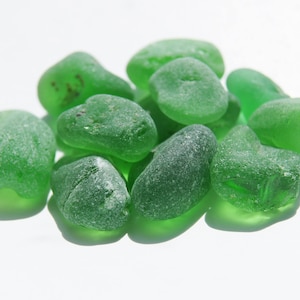 May include: A collection of smooth, green glass stones. The stones are various sizes and shapes, and they have a translucent quality.
