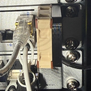 May include: A close-up of a network switch with a beige and brown plastic module plugged into the side. The switch has a black plastic casing with a silver metal faceplate. The faceplate has a label that says "RESET".