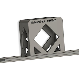Puede incluir: Un dispositivo gris y geométrico con el texto "NetworkBuck HMG-01" en la parte superior. Tiene una base rectangular y un diseño cuadrado de centro abierto con recortes en forma de diamante. La forma general es angular y moderna.