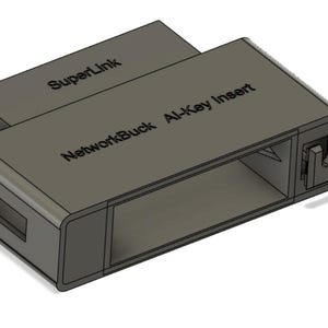 Puede incluir: Un dispositivo rectangular gris con el texto "NetworkBuck Al-Key Insert" y "SuperLink" impreso. El dispositivo tiene una ranura en un lado y un conector en el otro. Parece ser un componente de red o electrónico.