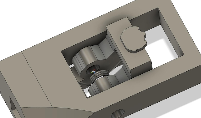 May include: A 3D-rendered mechanical component in shades of gray. The design features a central cylindrical element with a threaded screw, housed within a rectangular frame. A circular piece is visible on the right side, and the overall structure suggests a functional, possibly industrial, part.