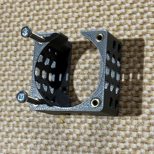 May include: A gray 3D-printed bracket with a semi-circular design and multiple small holes. Two silver screws are inserted through the bracket. The bracket is designed to hold an object, with a curved section and a rectangular section.