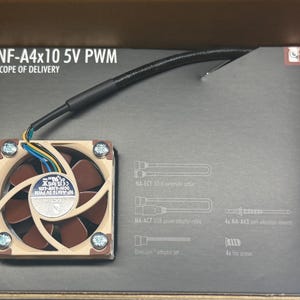 May include: A small computer fan with a brown and beige color scheme, featuring a central fan and a square frame. The fan is connected to wires and is packaged in a cardboard box. Text on the box reads "NF-A4x10 5V PWM SCOPE OF DELIVERY."
