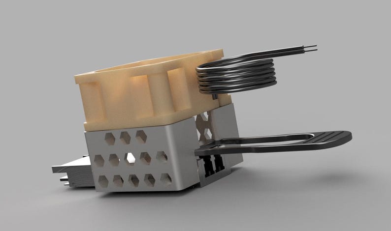 May include: A close-up of a mechanical component with a beige plastic housing, a silver metal frame with hexagonal cutouts, and a coiled wire element. A black plastic arm extends from the frame. The component is set against a gray background.