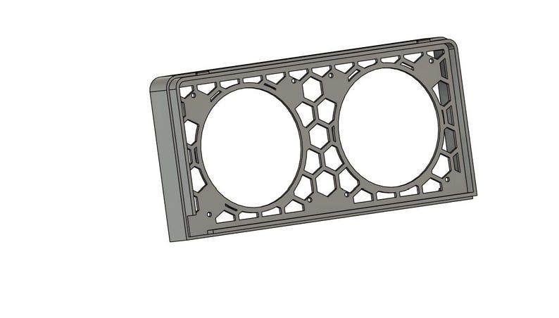 May include: A gray rectangular frame with two large circular openings. The frame has a honeycomb pattern and geometric cutouts. The design is a 3D rendering, likely for a product like a speaker grill or decorative panel.