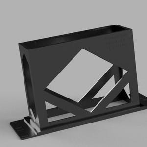 May include: A black geometric desk organizer with a rectangular base and a slanted, open-sided compartment. The design includes a large, angled cutout and text on the side. The organizer is made of a solid, matte material.