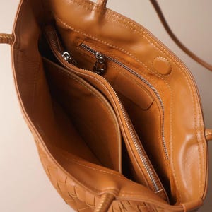 Puede incluir: Vista abierta de un bolso tote de cuero color marr&oacute;n claro. El bolso presenta un dise&ntilde;o tejido en el exterior y m&uacute;ltiples compartimentos interiores. Se ven cremalleras plateadas y un asa trenzada. El bolso est&aacute; vac&iacute;o.