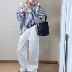 Puede incluir: Un atuendo casual que presenta una parte superior a rayas azules y blancas con mangas largas y cordones blancos. El atuendo incluye pantalones blancos de pierna ancha, un cintur&oacute;n negro y un bolso tote negro tejido. El atuendo se completa con zapatos estampados.