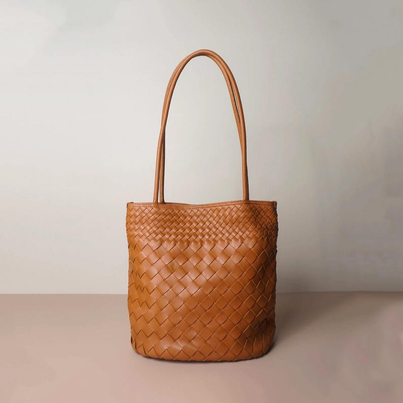 Puede incluir: Un bolso tote de cuero color canela con un dise&ntilde;o tejido. El bolso tiene dos asas largas y una forma rectangular. El bolso est&aacute; hecho de cuero marr&oacute;n claro.