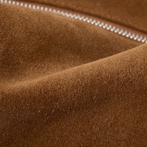 May include: Close-up of brown suede fabric with a silver zipper. The suede has a soft, textured appearance with subtle variations in color. The zipper is visible along the top edge, adding a contrasting element to the design.