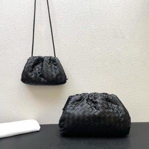 以下が含まれることがあります： 黒い革の編み込みハンドバッグが2つ。1つは細いストラップが付いた小さなクロスボディバッグです。もう1つは、より大きなクラッチバッグです。どちらのバッグもギャザーのトップと柔らかく丸みを帯びた形をしています。バッグは白い壁を背景に展示されています。