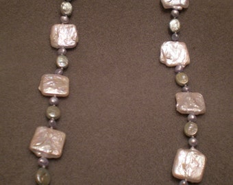 May include: A white pearl necklace with square-shaped pearls and smaller, iridescent blue beads.