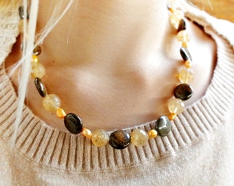 May include: A necklace made of round, faceted, golden and brown beads. The necklace is worn by a person with blonde hair.