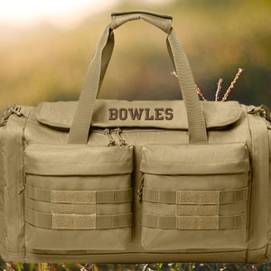 May include: A tan canvas duffel bag with multiple pockets and straps. The bag has the name "BOWLES" embroidered on the front.