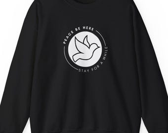 May include: Black sweatshirt with a white graphic of a dove inside a circle. The circle has the text "PEACE BE HERE" at the top and "STAY FOR A WHILE" at the bottom. The sweatshirt is a crew neck style.