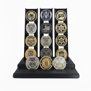 May include: A black display stand holding multiple collectible coins. The coins feature various emblems and text, including the FBI, SWAT, and other law enforcement or governmental organizations. The coins are in gold, silver, and bronze tones.