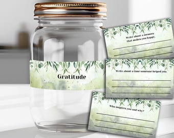 Könnte beinhalten: Ein Glasgefäß mit einem goldenen Deckel und einem grün-weißen Etikett mit der Aufschrift "Gratitude". Es gibt drei Karten mit grün-weißen Aquarelldesigns und Aufforderungen zum Schreiben über Dankbarkeit.