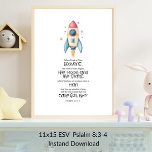 Könnte beinhalten: Gerahmter Druck mit einer Aquarellillustration einer Rakete in Rot, Blau und Gelb. Der Druck enthält einen Bibelvers aus Psalm 8:3-4. Der Rahmen ist hell und der Druck misst 28x38 cm.