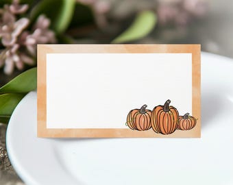 Puede incluir: Una tarjeta de sitio rectangular con un panel central blanco enmarcado por un borde de acuarela naranja claro. La esquina inferior derecha del espacio blanco está decorada con una ilustración de tres calabazas naranjas con tallos y enredaderas verdes.