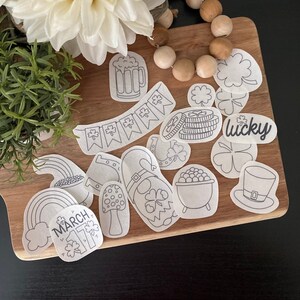 May include: A set of 14 black and white printable St. Patrick's Day themed stickers. The stickers include a pot of gold, a leprechaun, a shamrock, a horseshoe, a beer mug, a rainbow, a hat, and a banner that says "lucky".