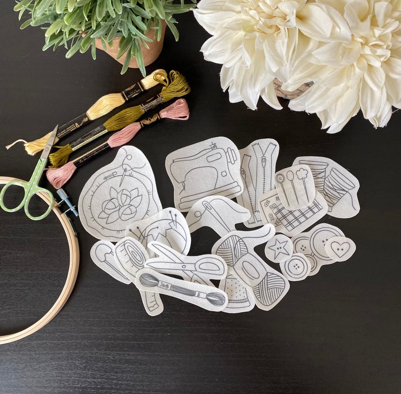 Op de afbeelding: Een set van 14 witte strijktransfers voor borduurprojecten. De ontwerpen omvatten een naaimachine, een rits, een naald en draad, een spoel draad, een knoop, een hart, een bloem en andere naai-gerelateerde items.