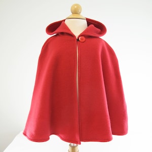 May include: A red hooded cape with a single button closure. The cape is made of a soft, plush fabric.