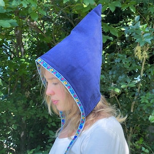May include: A royal blue, pointed hat with a floral trim. The hat is made of a soft fabric and has a decorative band of colorful flowers and leaves around the edge. The hat is a unique accessory.