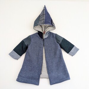 May include: A patchwork coat with a pointed hood. The coat is primarily blue with contrasting fabric patches on the sleeves and hood. The hood lining features a white and black polka dot pattern. The coat has a zipper closure.