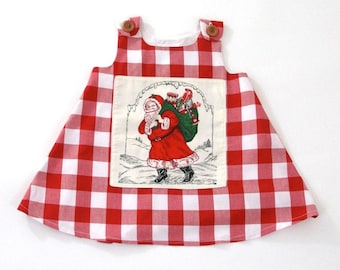 Könnte beinhalten: Ein rot-weiß kariertes Weihnachts-Kleid mit einem Weihnachtsmann-Motiv. Das Kleid hat Holzknöpfe an den Schultern und ein weißes Futter. Das Weihnachtsmann-Motiv zeigt den Weihnachtsmann mit einem Sack voller Spielzeug.
