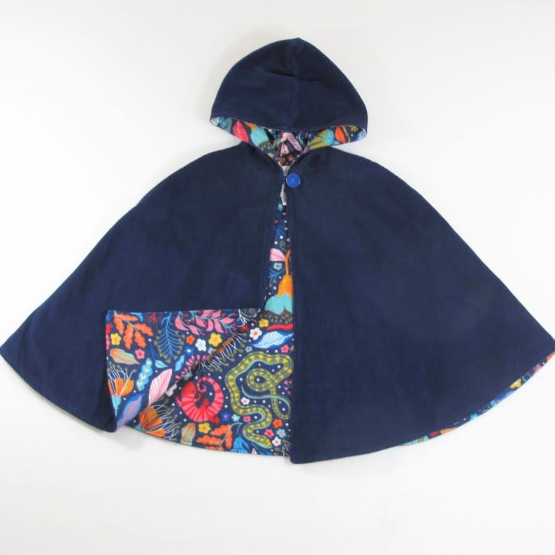 May include: A navy blue hooded cape featuring a single blue button closure at the neck. The interior lining displays a vibrant, multicoloured botanical and serpentine pattern with orange, pink, yellow, and green elements against a dark blue background.