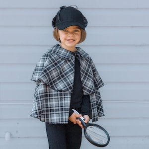 May include: A black deerstalker hat, a black long-sleeved shirt, black trousers, and a grey and black plaid cape with a collar. A black magnifying glass is held in the hand. The outfit is designed for a detective costume, featuring a classic pattern.