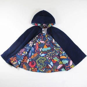 May include: A hooded cape featuring a solid dark navy blue exterior and a vibrant interior lining. The lining displays a colourful botanical pattern with illustrations of lizards, snakes, and various tropical flowers in shades of red, orange, yellow, and blue.
