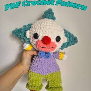 Peut inclure: Une poupée clown en peluche faite de fil doux avec une tête blanche, des cheveux bleu sarcelle, un nez rouge et une bouche rose. La poupée porte une chemise violette avec un nœud papillon bleu et un pantalon vert avec des pieds rouges.