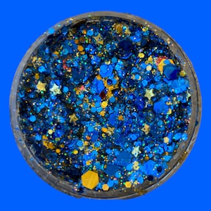 May include: A clear container filled with a mix of blue, gold, and iridescent glitter. The glitter includes various shapes like stars and hexagons, creating a sparkling effect. The container is set against a bright blue background.