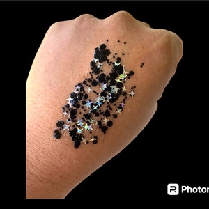 May include: Black and iridescent glitter in the shape of stars and small circles on a hand.
