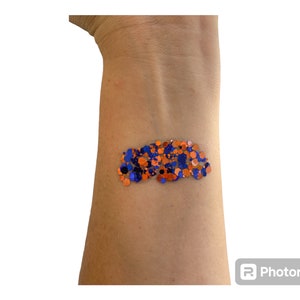 May include: A close-up of a person's arm with a cluster of blue and orange glitter on the skin.