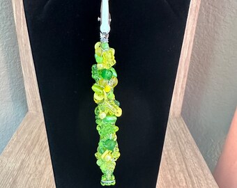 May include: A green and yellow glass bead necklace with a silver clasp. The necklace is displayed on a black velvet stand.