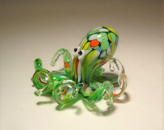 May include: A green glass octopus figurine with white, red, orange, and blue accents. The octopus has eight tentacles and large, black eyes.