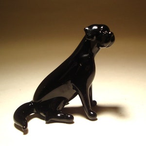 May include: A black glass figurine of a dog sitting with its head turned to the side. The dog has a short, smooth coat and a short tail.