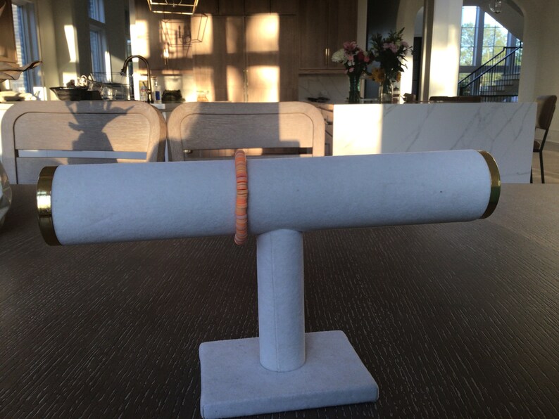 K&ouml;nnte beinhalten: Ein wei&szlig;er Schmuckst&auml;nder mit goldener Verzierung, auf dem ein Armband aus Korallen- und wei&szlig;en Perlen liegt.