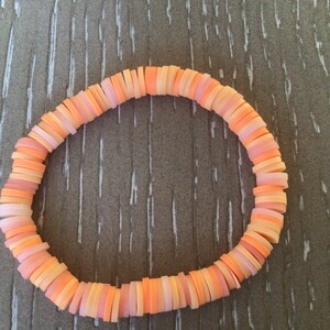 K&ouml;nnte beinhalten: Ein Armband aus &uuml;bereinander gestapelten, runden Perlen in Pfirsich- und Oranget&ouml;nen.