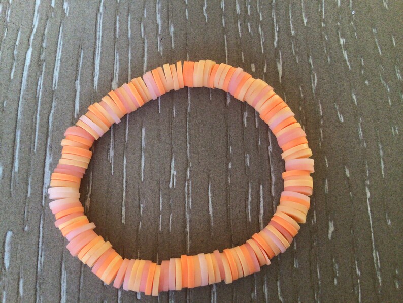 K&ouml;nnte beinhalten: Ein Armband aus &uuml;bereinander gestapelten, runden Perlen in Pfirsich- und Oranget&ouml;nen.