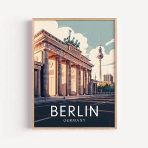 May include: A framed art print featuring the Brandenburg Gate in Berlin, Germany. The artwork depicts the iconic landmark with a light blue sky, clouds, and the Berlin TV Tower in the background. The word "BERLIN" is printed in white.