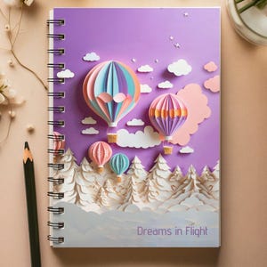 Puede incluir: Un cuaderno con espiral con una cubierta morada que presenta un diseño de arte en papel de globos aerostáticos, nubes y árboles. El cuaderno tiene el texto "Dreams in Flight" en la parte inferior. Un lápiz y flores están en el fondo.