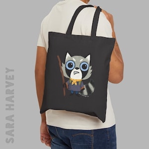 May include: Black tote bag featuring a cartoon raccoon character with blue eyes, a yellow scarf, and a wooden stick. The raccoon is wearing a blue shirt and gray fur. The bag has black handles and the text "SARA HARVEY" printed vertically on the side.