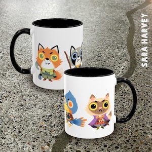 May include: Two white ceramic mugs with black interiors and handles. Each mug features colorful cartoon animal illustrations. One mug has a fox and raccoon, the other has a bird and cat. The artist's name, Sara Harvey, is printed vertically on the right.