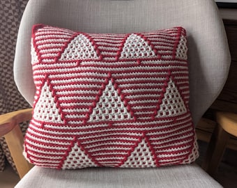 May include: A square crochet pillow featuring a repeating geometric pattern of white triangles set against a background of horizontal red and white stripes. The textured yarn construction creates a raised effect for the triangular shapes.