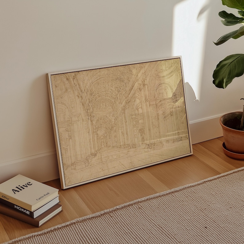 Op de afbeelding: Een ingelijste architectuurprint in een licht houten frame. De print toont een gedetailleerde schets van een kathedraalinterieur in beige en bruine tinten. Het kunstwerk leunt tegen een witte muur op een houten vloer, met boeken en een plant in een pot in de buurt.