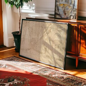 Op de afbeelding: Een ingelijste architecturale tekening met een zwart frame, die een gedetailleerd interieur van een kathedraal toont. De tekening is in beige en bruine tinten. Het kunstwerk leunt tegen een houten kast, met een rood tapijt op de voorgrond.