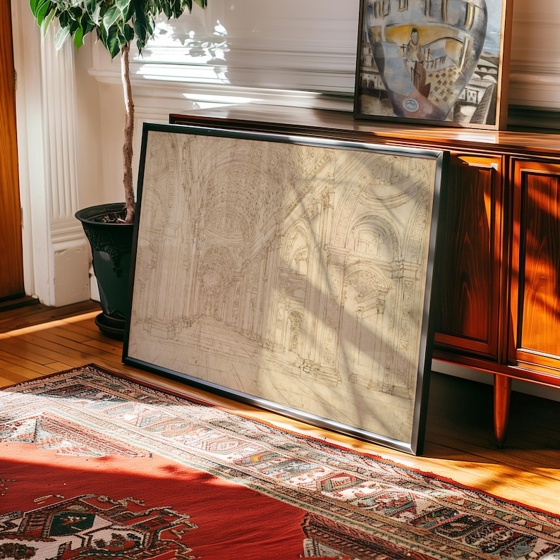 Op de afbeelding: Een ingelijste architecturale tekening met een zwart frame, die een gedetailleerd interieur van een kathedraal toont. De tekening is in beige en bruine tinten. Het kunstwerk leunt tegen een houten kast, met een rood tapijt op de voorgrond.